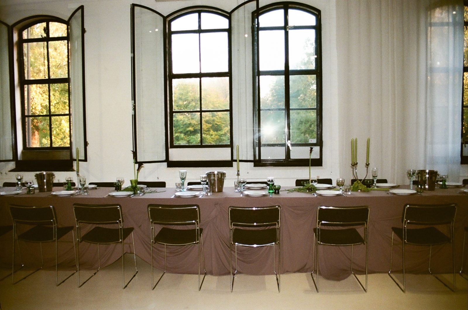 A long dinner table set for a private dinner in front of the arched warehouse windows