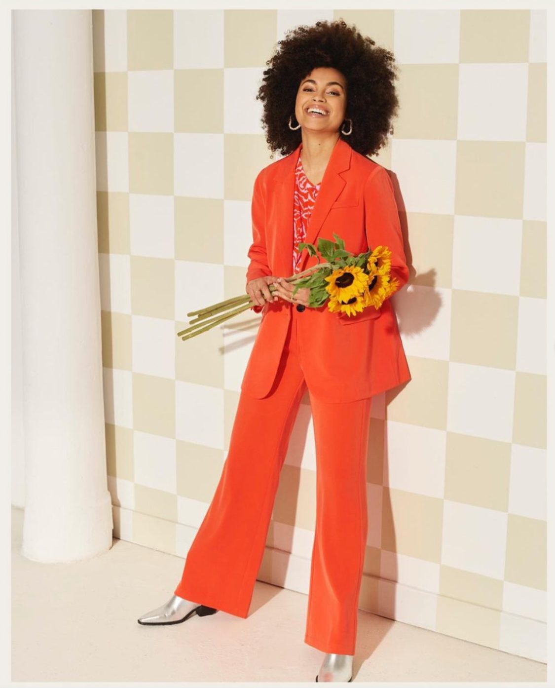 Editorial fashion work — model in an orange suit with sunflowers on the checker wall