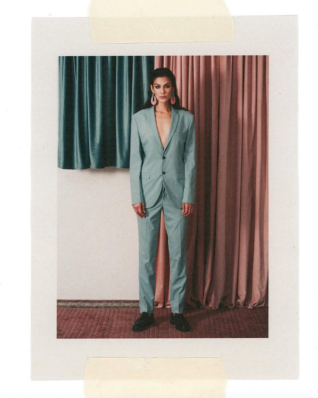 Editorial fashion work — model in a light blue suit between pink and green curtains