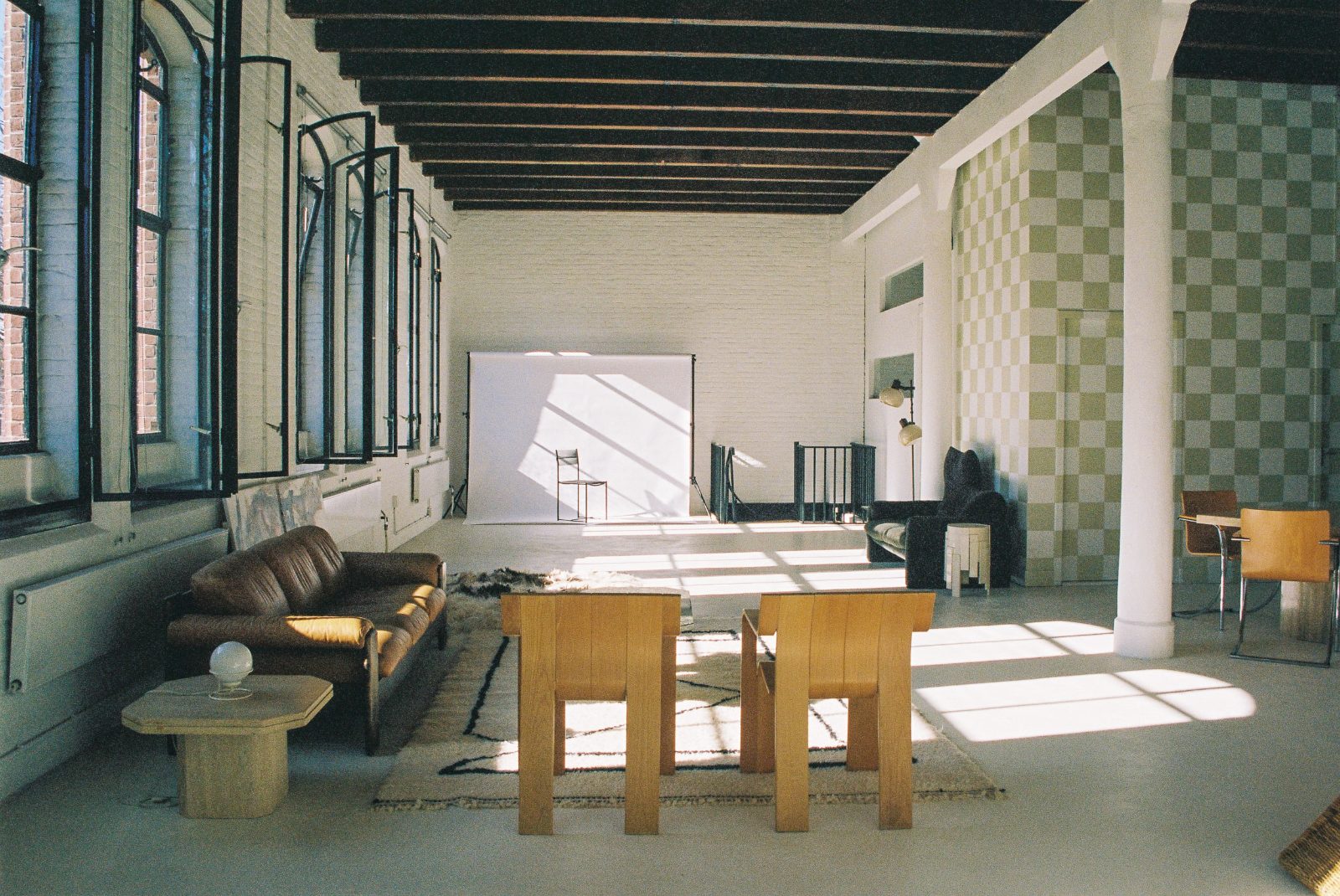 The full studio — wooden table, vintage sofa and white brick under the beams